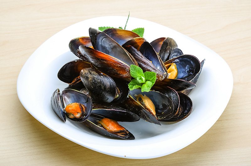 Fresh tasty Boiled mussels with herbs on wood background